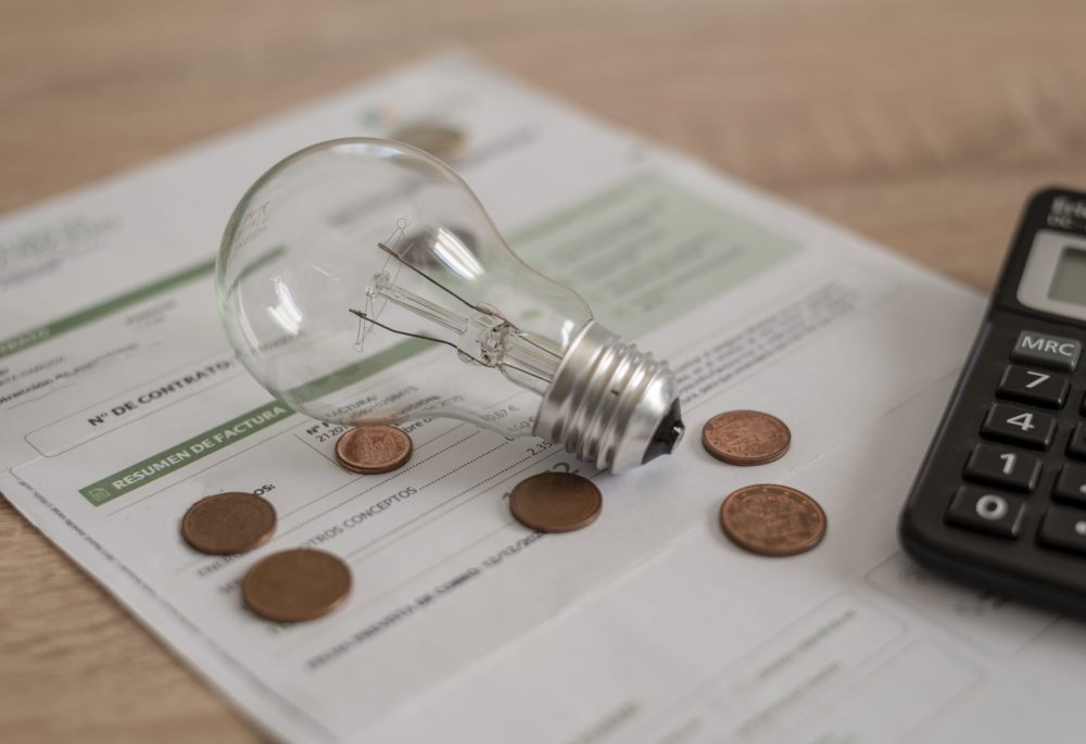 Electricity bill with light bulb, several coins and calculator on the desk. Concept of electricity prices and tax payments