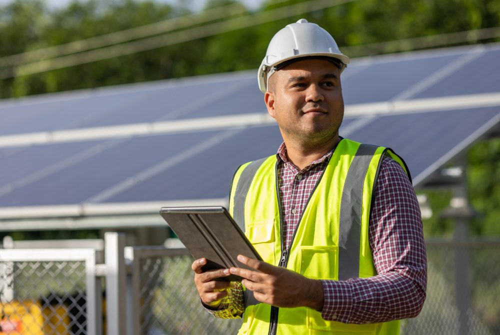 Young asian electrical engineer standing in front of Solar cell panels farm. He using tablet to checking the system. Solar generator power concept.